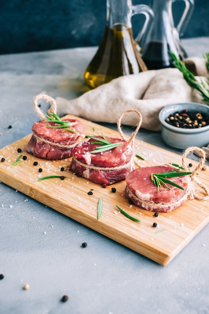 Filete mignon de ternera cruda sobre una tabla de madera con romero y especias.