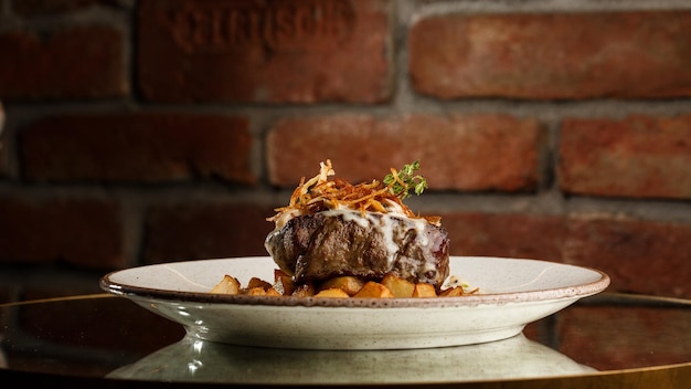 Filete a la parrilla con papas doradas al horno servido con cebolla crujiente encima sobre un fondo de ladrillo Deliciosa Receta