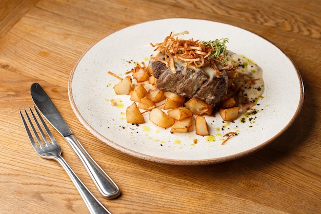 Filete a la parrilla con papas doradas al horno servido con cebolla crujiente encima sobre un fondo de ladrillo Deliciosa Receta