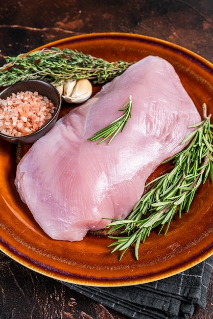 Filete de pechuga de pavo de ave cruda en un plato rústico con romero y tomillo