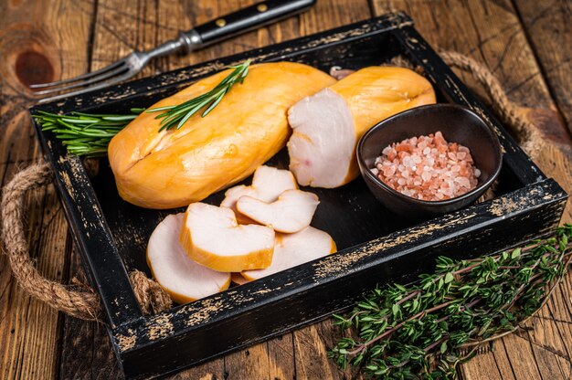 Filete de pechuga de pollo ahumado caliente sobre una tabla de madera con hierbas