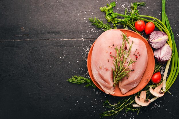 Filete de pechuga de pollo crudo con verduras frescas y romero y especias sobre un fondo de madera negra Vista superior Espacio libre para texto