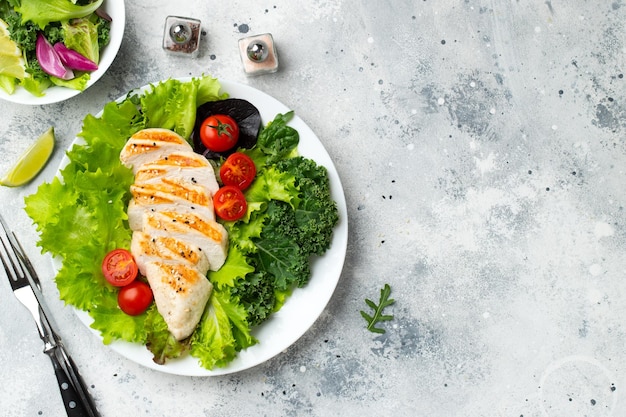 Filete de pechuga de pollo y ensalada de verduras con tomates y hojas verdes sobre un fondo claro El concepto de comida saludable y dieta cetogénica Vista superior con espacio de copia