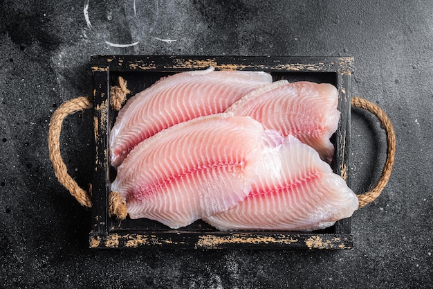 Filete de pescado blanco de tilapia fresca en una bandeja de madera Fondo negro Vista superior
