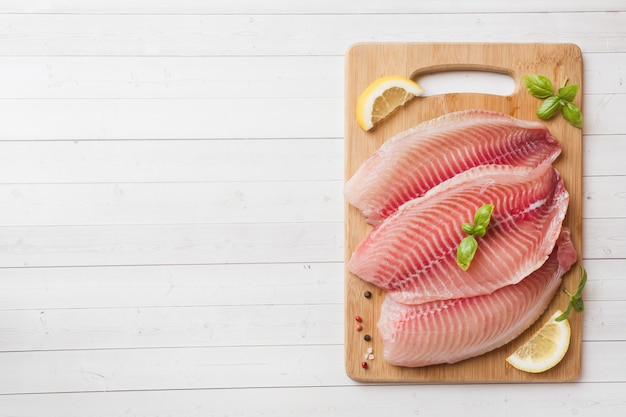 Filete de pescado crudo de tilapia en una tabla para cortar con limón y especias