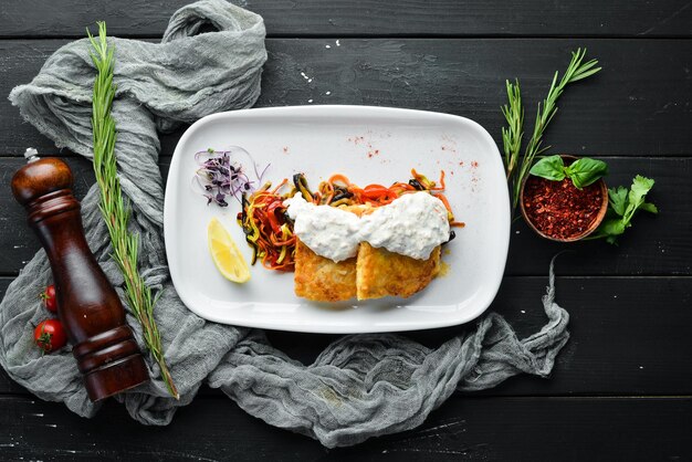 Filete de pescado frito con verduras en salsa cremosa En el plato Sobre un fondo de madera Vista superior Espacio libre para el texto