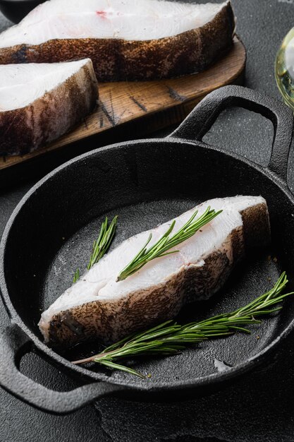 Filete de pescado de halibut fresco crudo, con ingredientes y hierbas de romero, sobre fondo de mesa de piedra oscura negra