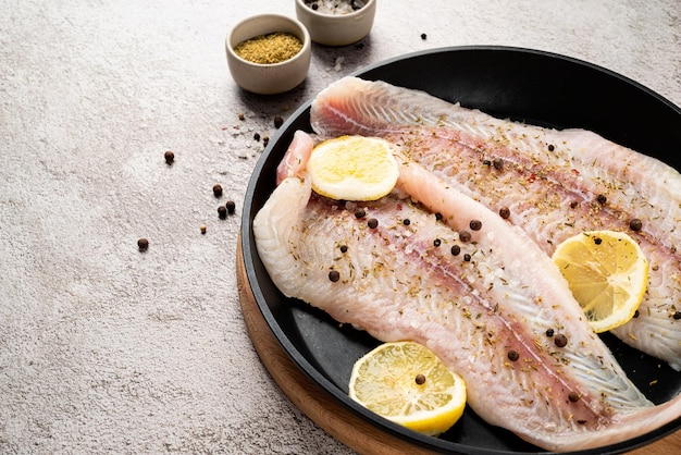 Filete de pescado pangasius crudo con limón y especias en sartén sobre fondo de hormigón