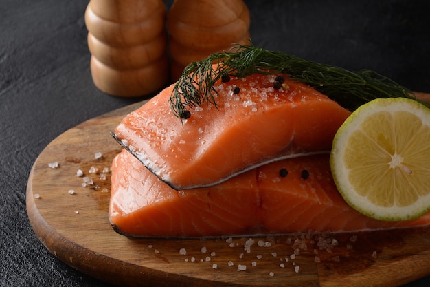 Filete de pescado de salmón crudo fresco con ingredientes de cocina hierbas y limón sobre fondo negro