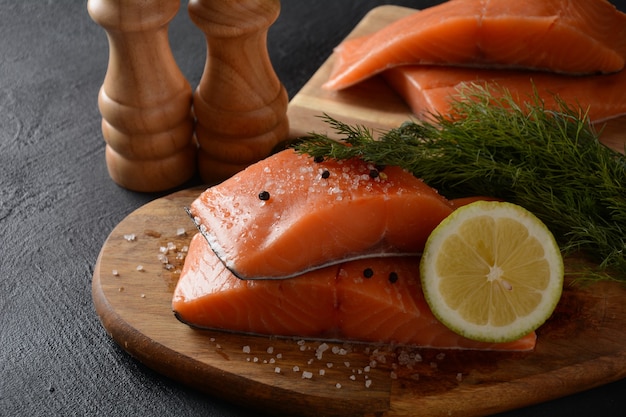 Filete de pescado de salmón crudo fresco con ingredientes de cocina hierbas y limón sobre fondo negro