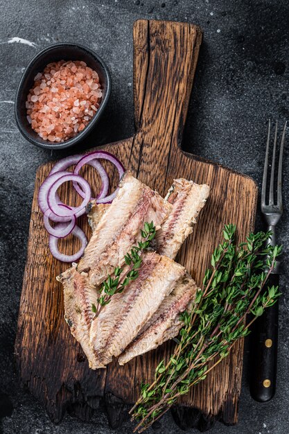 Filete de pescado de sardina en aceite de oliva sobre tabla de madera. Fondo negro. Vista superior.