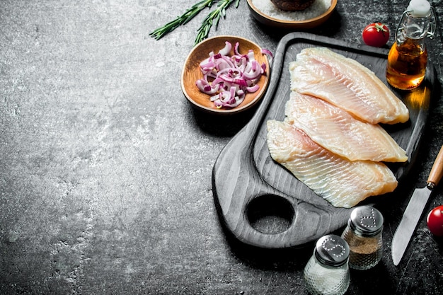 Filete de pescado en una tabla de cortar con cebolla picada en un bol y especias