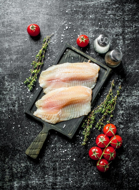 Filete de pescado en una tabla de cortar con especias de tomillo y tomates en una rama