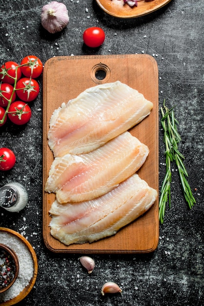 Filete de pescado en una tabla de cortar de madera con romero y tomates