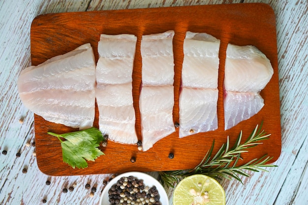 Foto filete de pescado en tablero de madera con ingredientes para cocinar filete de pescado pangasius crudo fresco con hierbas y especias pimienta negra lima limón y carne de romero pescado dolly tilapia bagre rayado