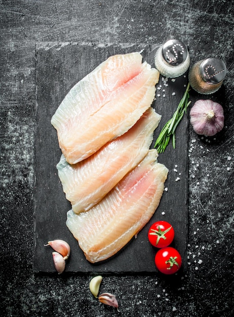 Filete de pescado tilapia en un tablero de piedra con tomates, dientes de ajo y especias