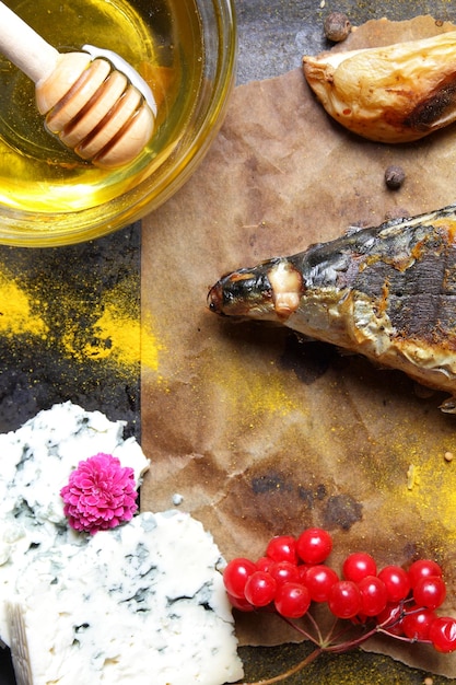 Filete de pescado con verduras, miel y queso azul sobre un fondo oscuro Caballa a la parrilla con bayas de limón y flores rosas sobre papel pergamino Primer plano