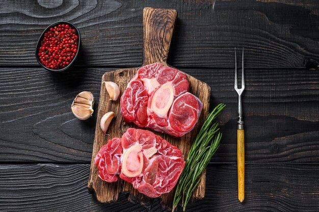 Filete de pierna de ternera osso buco de carne cruda, haciendo ossobuco italiano. Fondo de madera negra. Vista superior.