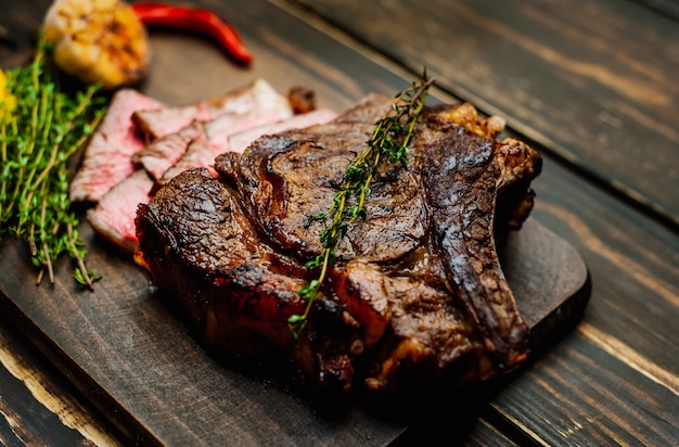 Filete a la plancha sobre tabla de cortar con limón, pimiento rojo, ajo y condimento en rústico oscuro