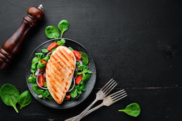 Filete de pollo al horno con verduras En un plato negro sobre un fondo de madera Vista superior Espacio libre para su texto Plano