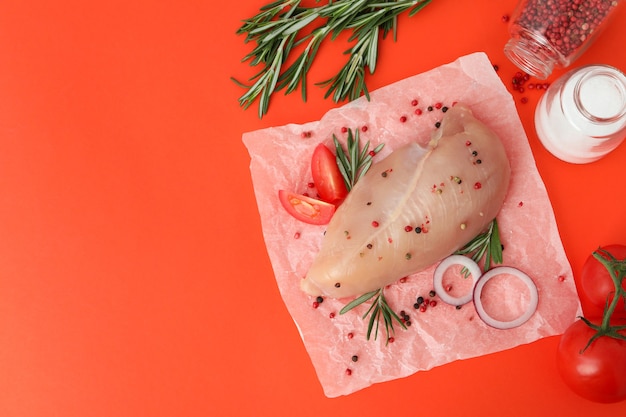 Filete de pollo crudo con ingredientes sobre fondo naranja