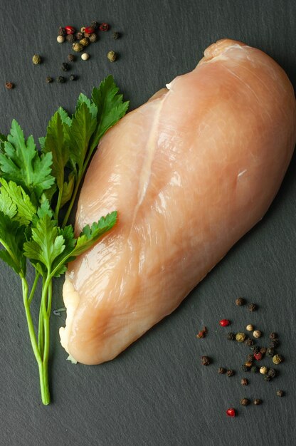 filete de pollo crudo sobre fondo negro con granos de pimienta y perejil ingredientes para cocinar carne para cocinar