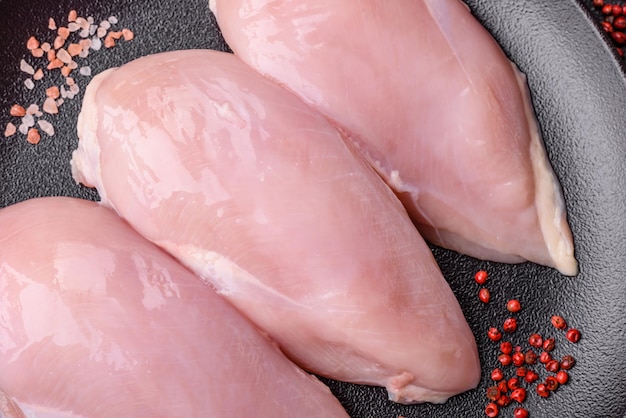 Filete de pollo fresco en una mesa de hormigón oscuro con especias y hierbas