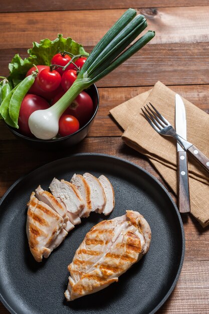 Filete de pollo a la plancha en sartén. Verduras crudas en un tazón, fondo de madera