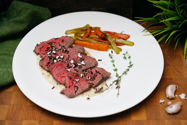 Foto filete de res en puré de pastinaca con zanahoria frita y palitos de apio en un plato blanco guarnición con arroz frito y tomillo