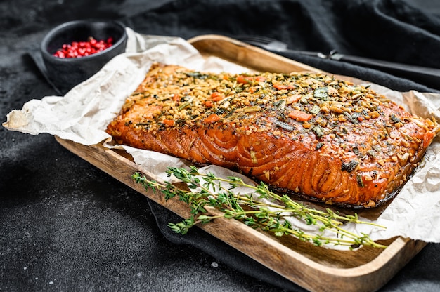 Filete de salmón ahumado caliente en una tabla de cortar. trucha. Fondo negro, vista desde arriba.