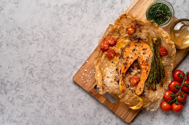 Foto filete de salmón al horno sobre pergamino con verduras, espárragos, tomates