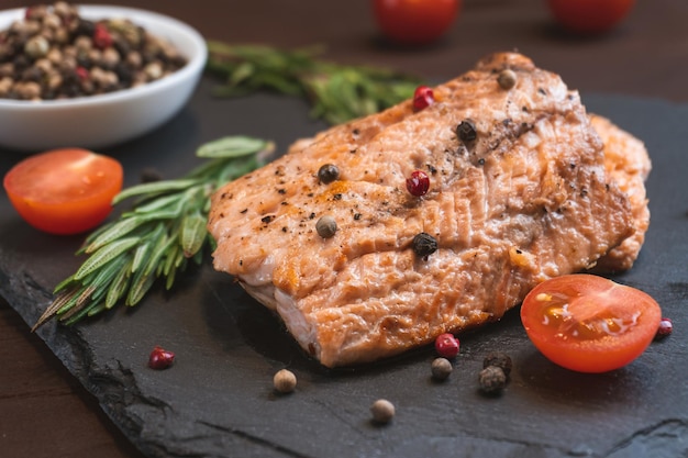 Filete de salmón de carne de pescado rojo a la parrilla con romero de tomate y especias sobre fondo de piedra negra