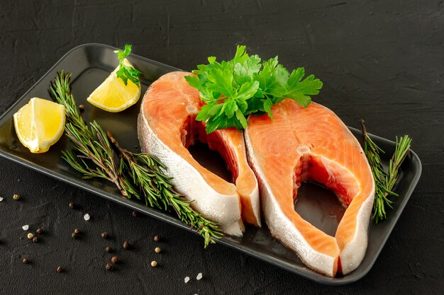 Filete de salmón crudo fresco con limón, romero, pimienta y perejil sobre fondo negro.