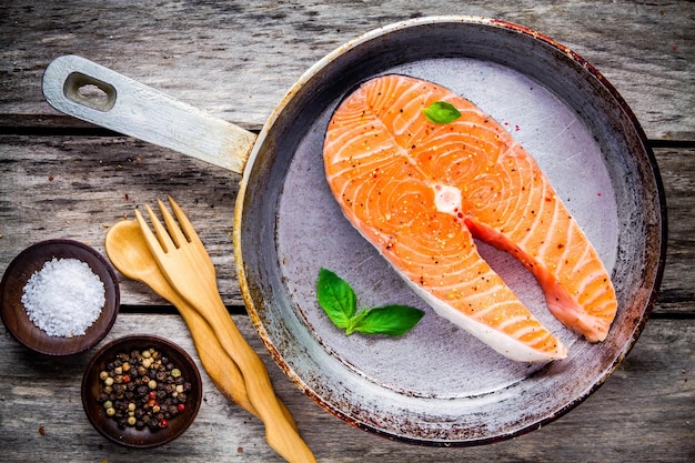 Filete de salmón crudo fresco en una sartén de hierro fundido con sal marina y pimientos en la mesa rústica de madera