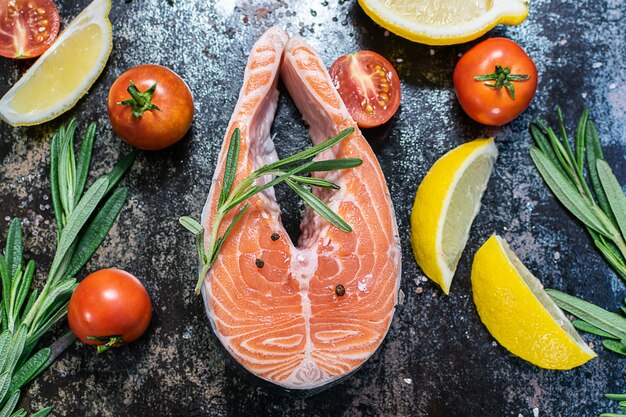 Filete de salmón crudo con verduras y hierbas en la vista superior de la mesa negra.