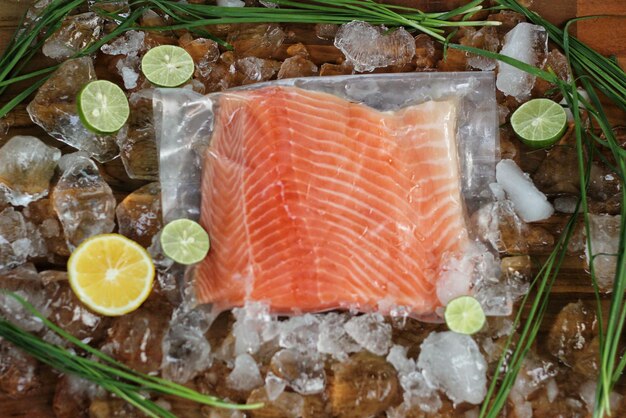 Foto filete de salmón fresco envasado para sashimi rodeado de trozos de hielo, limón y lima.