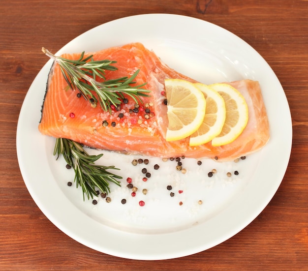 Filete de salmón fresco con hierbas y rodajas de limón sobre fondo de madera plateada