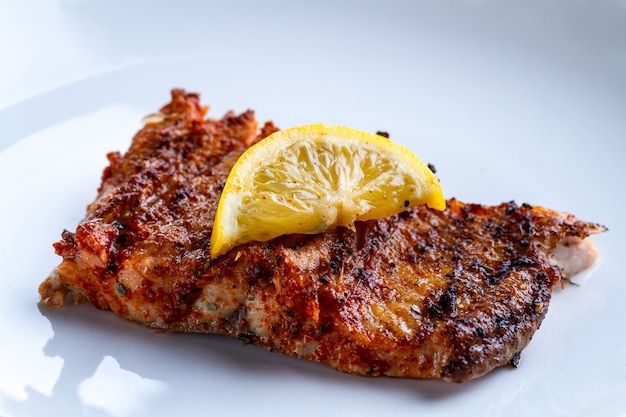 Filete de salmón fresco a la parrilla con una rodaja de limón jugoso en un plato blanco