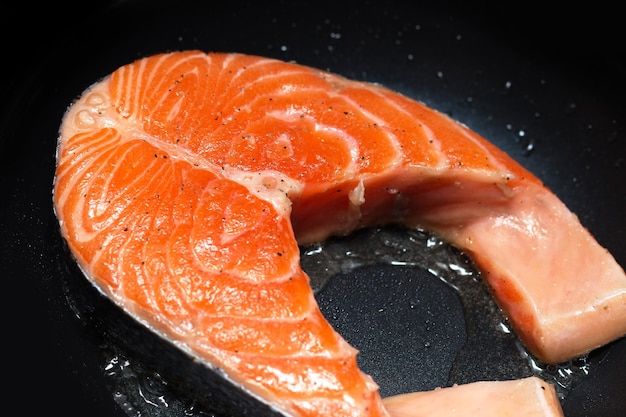 Filete de salmón fresco en una sartén negra frito en un poco de aceite.