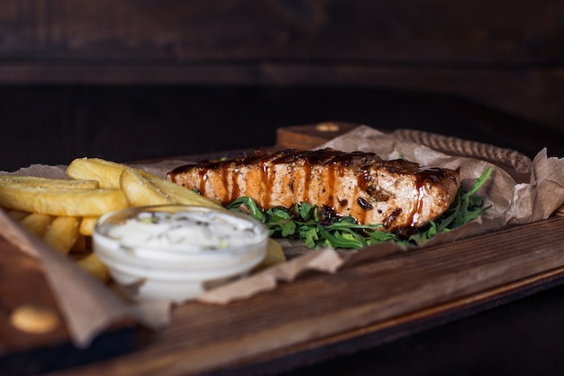 Filete de salmón con papas fritas en una bandeja de madera, hermosa porción, superficie oscura.