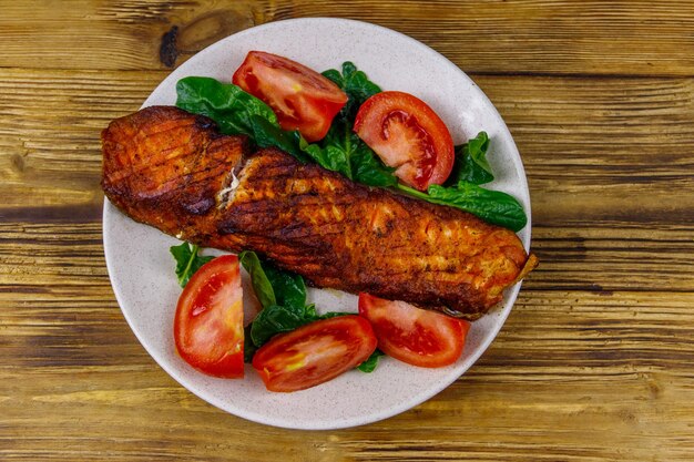 Filete de salmón a la parrilla con espinacas y tomates en la mesa de madera Vista superior