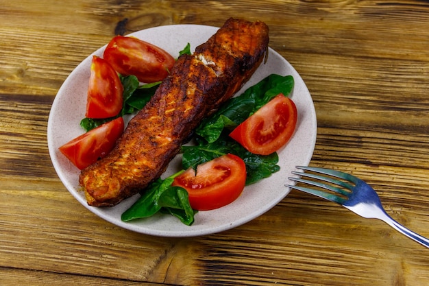 Filete de salmón a la parrilla con espinacas y tomates sobre mesa de madera