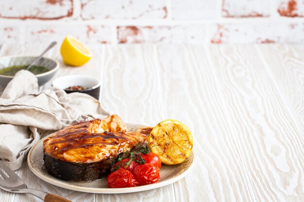 Filete de salmón a la parrilla glaseado con salsa teriyaki, verduras y limón servido en un plato de cerámica sobre una mesa de madera blanca rústica desde un ángulo de visión, enfoque selectivo con espacio para texto