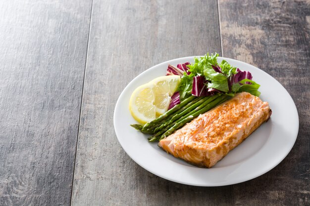 Filete de salmón a la plancha con espárragos y ensalada en la mesa de madera Copia espacio