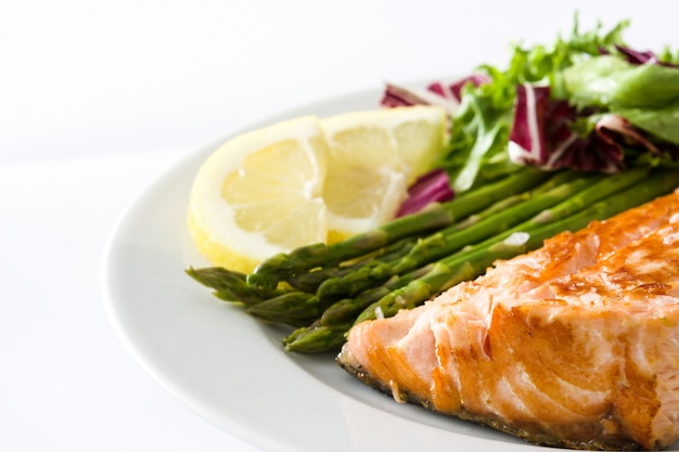 Filete de salmón a la plancha con espárragos y ensalada en plato aislado en blanco