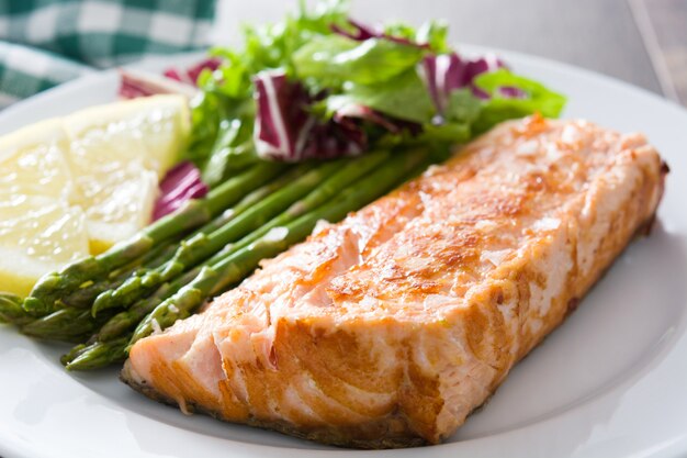 Filete de salmón a la plancha con espárragos y ensalada en plato sobre mesa de madera