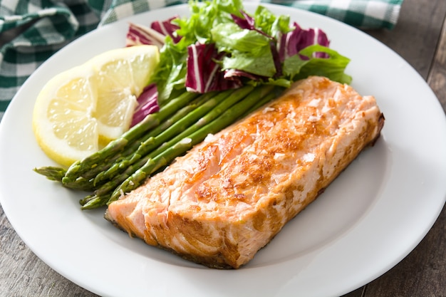 Filete de salmón a la plancha con espárragos y ensalada en plato sobre mesa de madera