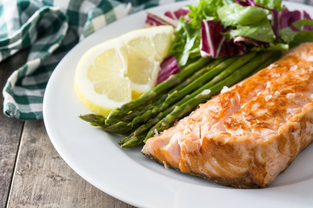 Filete de salmón a la plancha con espárragos y ensalada en plato sobre mesa de madera