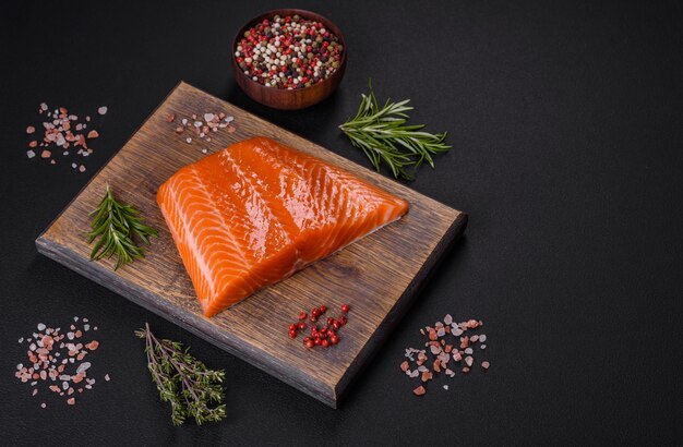 Filete de salmón rojo crudo con especias saladas y hierbas sobre un fondo de hormigón oscuro