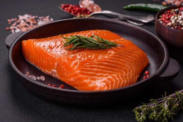 Filete de salmón rojo crudo con especias saladas y hierbas sobre un fondo de hormigón oscuro